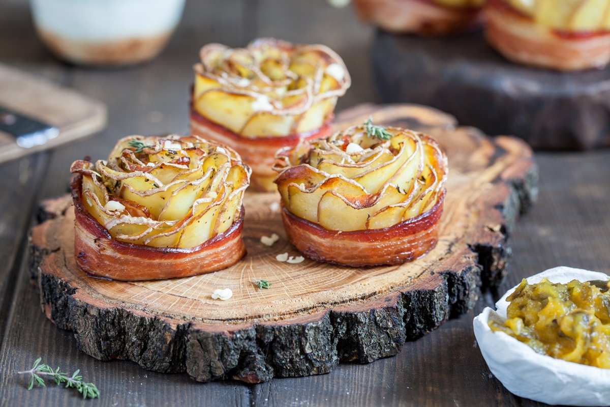 Trei trandafiri crocanți din cartofi cu bacon pe un platou rustic de lemn, alături de un bol cu salată de murături