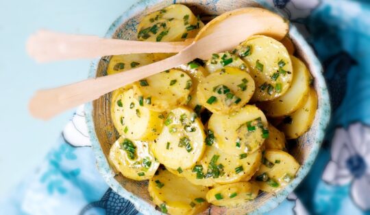 Salată de cartofi cu usturoi verde în bol de servire cu două linguri de lemn