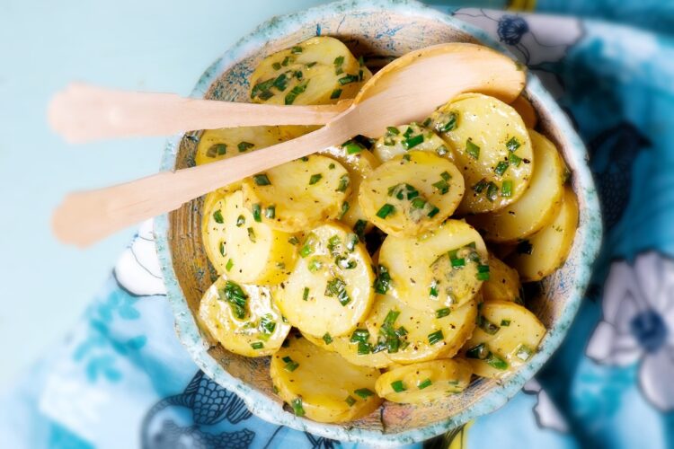 Salată de cartofi cu usturoi verde în bol de servire cu două linguri de lemn