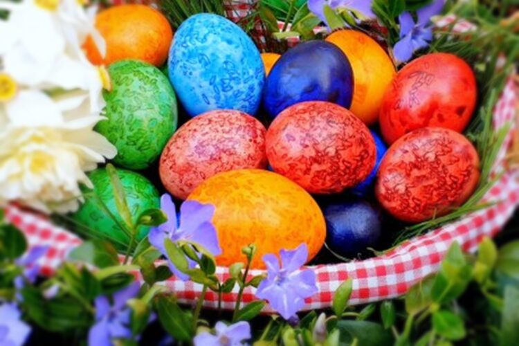 Ouă vopsite cu tehnica orezului și coloranți alimentari într-un coș așezat printre flori