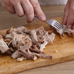 Carnea se desface în franjuri cu furculița pe un tocător