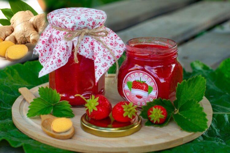Două borcane cu gem de căpșuni aromat cu ghimbir, alături de căpșuni proaspete și ghimbir feliat