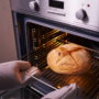 De ce crapă pâinea în cuptor ilustrată cu ajutorul a două mâini care pun o pâine în cuptor