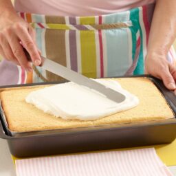 Femeie întinzând crema de mascarpone cu o spatulă peste blatul de prăjitură