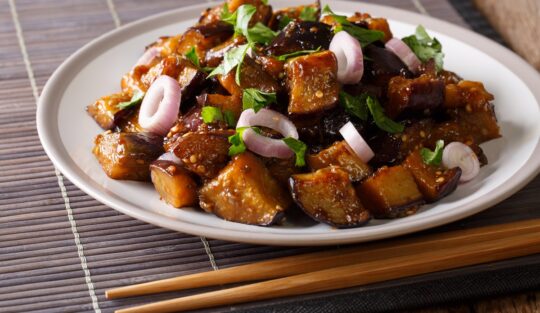 Porție de vinete chinezești cu sos de usturoi și sos de soia într-o farfurie și două bețe de servit