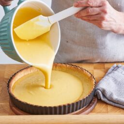 Femeie adăugând cremă de vanilie în interiorul crustei de tartă