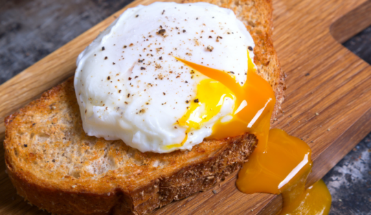 Un ou poșat servit pe o felie de pâine prăjită care stă pe un blat de lemn