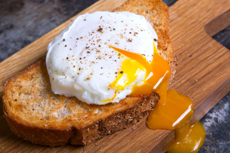 Un ou poșat servit pe o felie de pâine prăjită care stă pe un blat de lemn