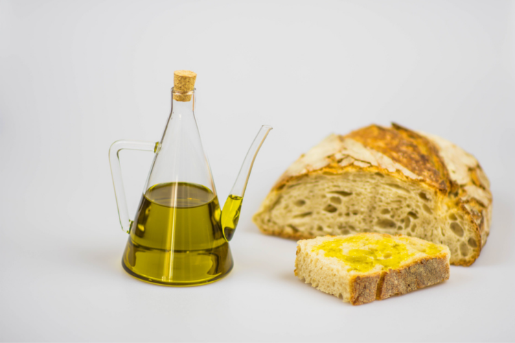 O sticlă cu ulei de măsline alături de mai multe felii de pâine pentru a ilustra cum se degustă uleiul de măsline