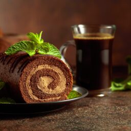 Ruladă cu cremă de cafea și mascarpone. pe o farfurie, decorată cu frunze de mentă și o ceașcă de cafea