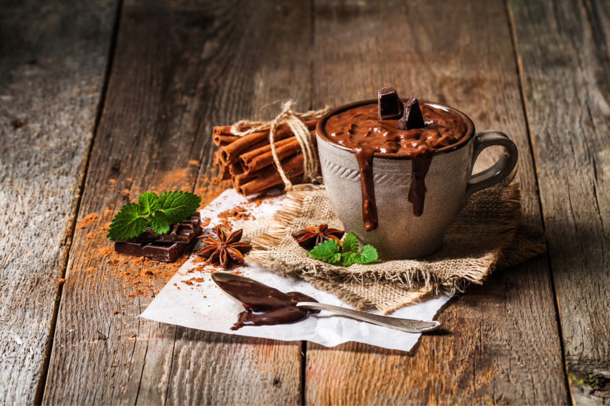 ciocolata caldă servită într-o ceașcă argintie alături de câteva bezele