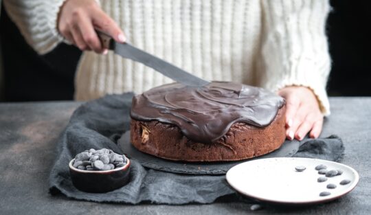 Femeie întinzând glazura de ciocolată cu o spatulă peste prăjitură