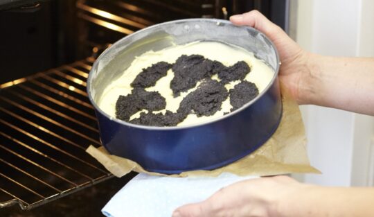 Femeie introducând în cuptor tava cu blat pentru tort cu compot de dovleac și blat marmorat cu mac