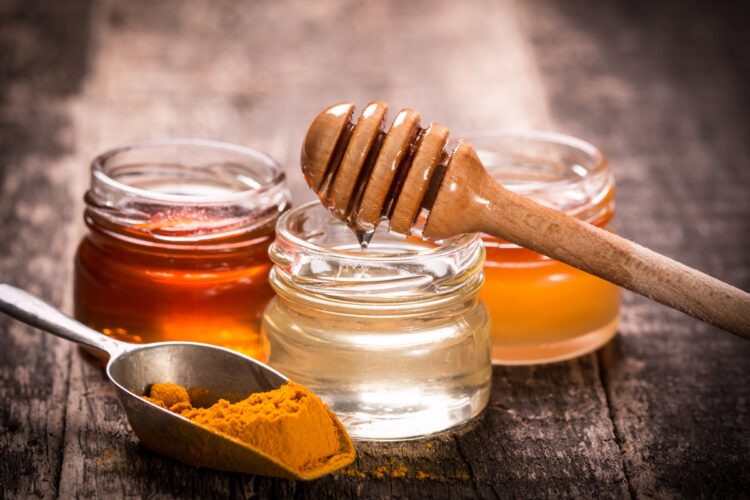 Borcane cu Curcuma cu miere sau miere de aur, alături de un borcan cu apă, o ustensilă de miere și o lingură cu pudră de curcuma
