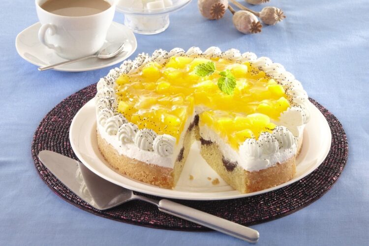 Tort cu compot de dovleac și blat marmorat cu mac porționat pe platou, alături de o spatulă de tort, o ceașcă cu cafea și tulpini de mac