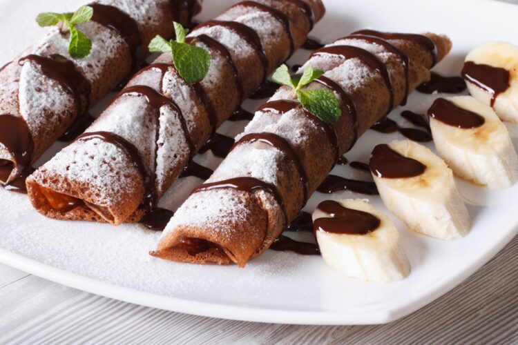 Clătite cu ciocolată și banane decorate cu zahăr pudră și cu frunze de mentă