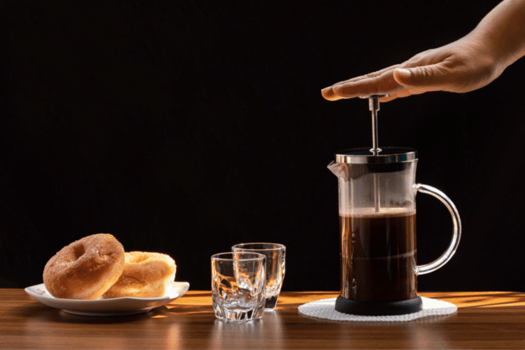 O mână care folosește o presă franceză pentru a prepara cafea