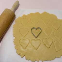 Aluat de biscuiți decupat cu o formă de inimioară, alături de un sucitor de aluaturi