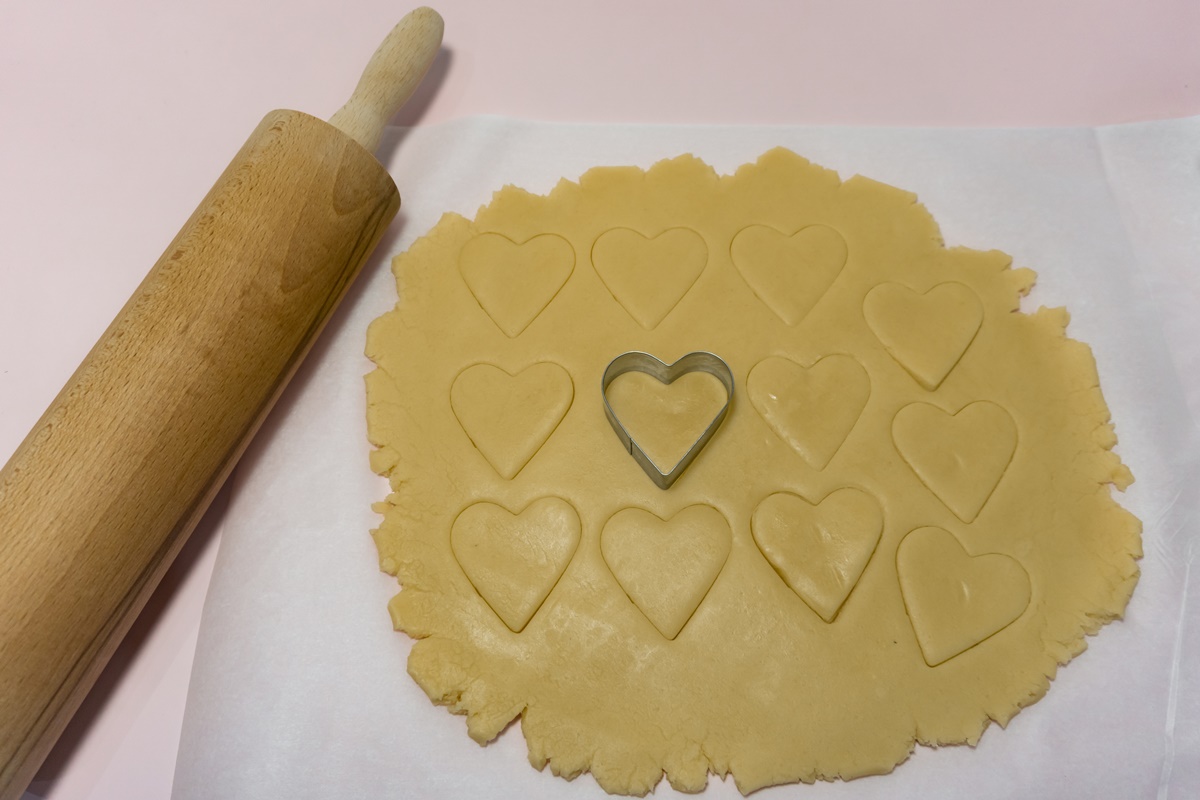 Aluat de biscuiți decupat cu o formă de inimioară, alături de un sucitor de aluaturi