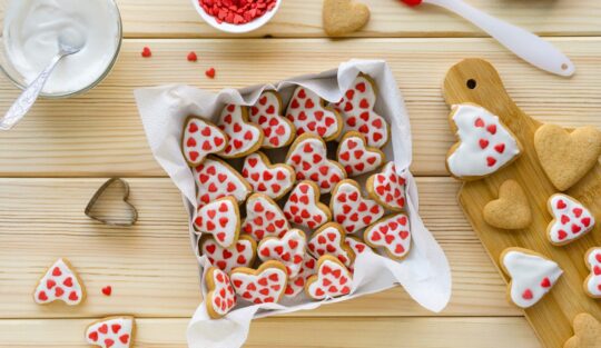 Biscuiți cu glazură albă și inimioare roșii într-o tavă cu hârtie de copt
