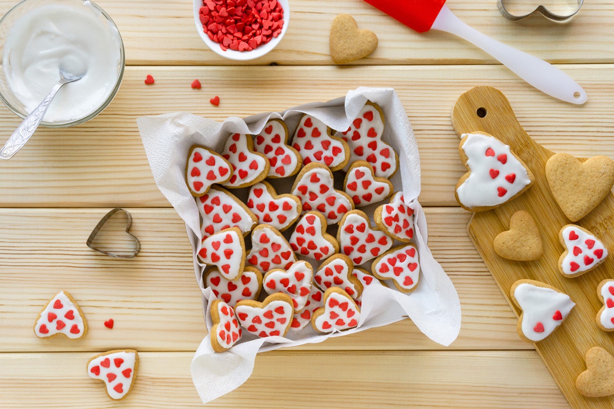 Biscuiți cu glazură albă și inimioare roșii într-o tavă cu hârtie de copt