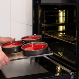 Bărbat introducând în cuptor tava cu prăjituri roșii