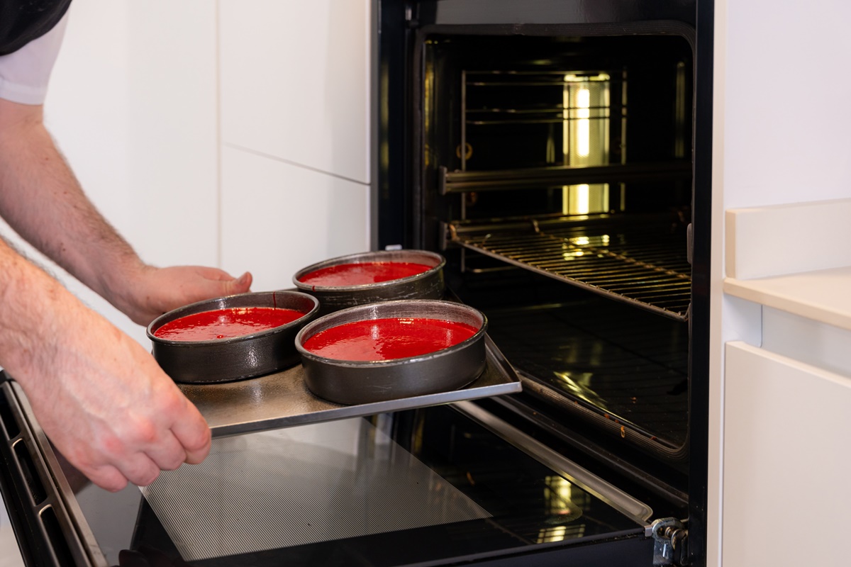 Bărbat introducând în cuptor tava cu prăjituri roșii