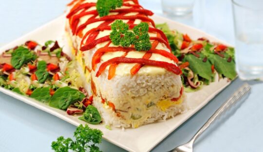 Terină de orez cu ton și ardei copți pe un platou alb, cu salată de crudități