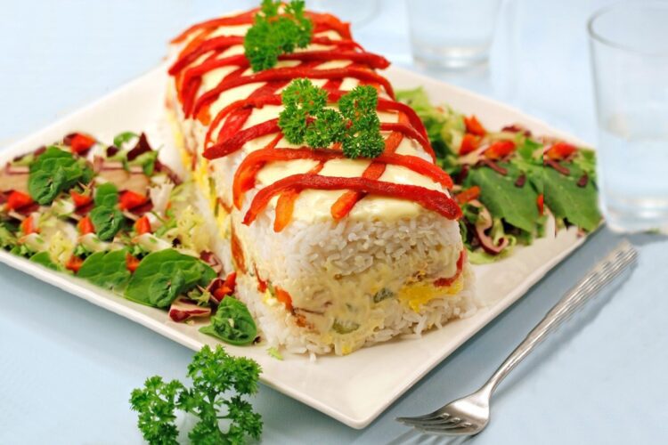 Terină de orez cu ton și ardei copți pe un platou alb, cu salată de crudități