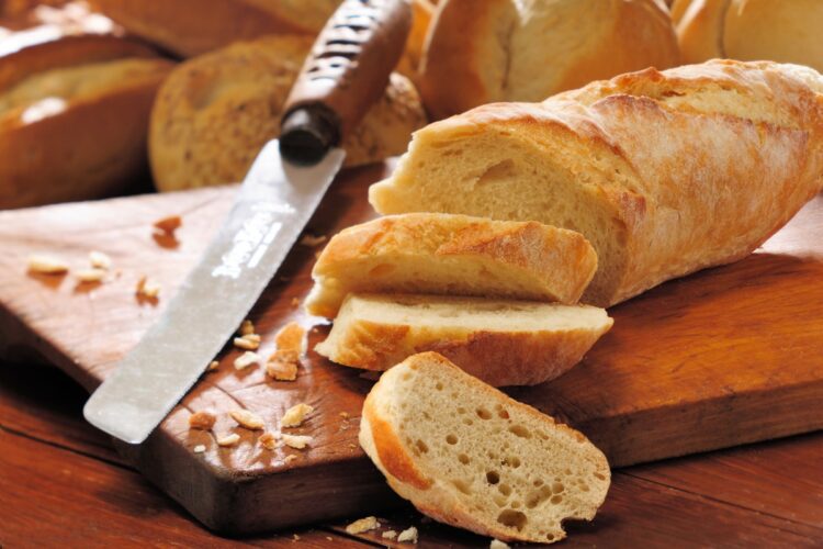 Baghetă de pâine feliată pe un tocător de lemn, alături de un cuțit