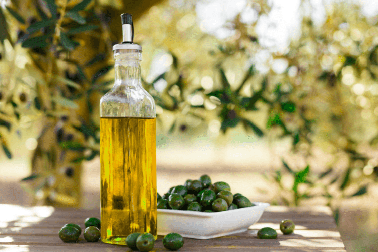 O sticlă cu ulei de măsline alături de o farfurie plină cu măsline negre