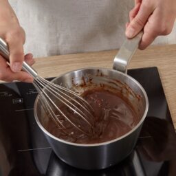 Persoană amestecând cu telul în cratița cu glazură de ciocolată