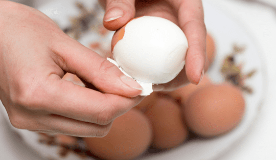 Două mâini de femeie care curăță un ou de coajă