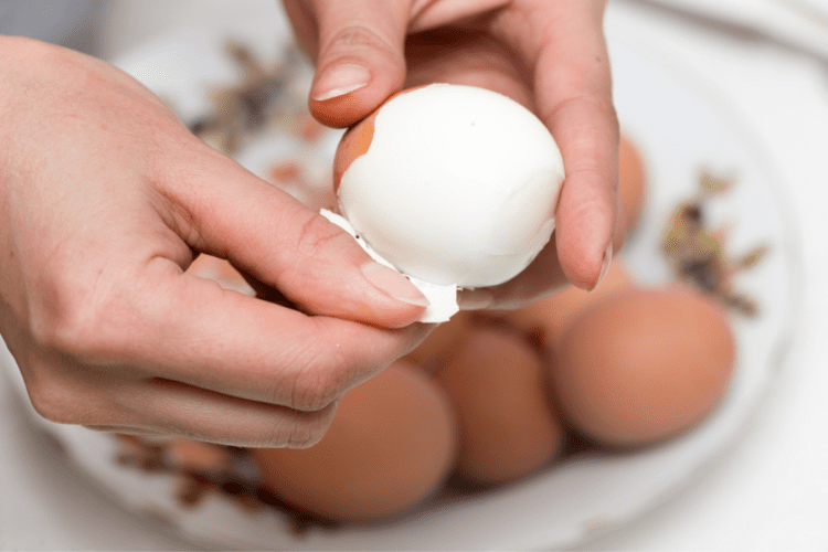 Două mâini de femeie care curăță un ou de coajă