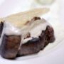 O bucată de steak de vită, cu un sos de smântână, șezate pe o farfurie albă, adâncă